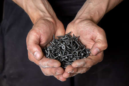 Black small self tapping screws for steel profile of drywall on young adult man hand on light gray table background. Opened palm. Closeup.の写真素材