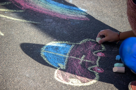 girl draws a rainbow, sun, car with chalk on the asphalt. Selective focusの写真素材