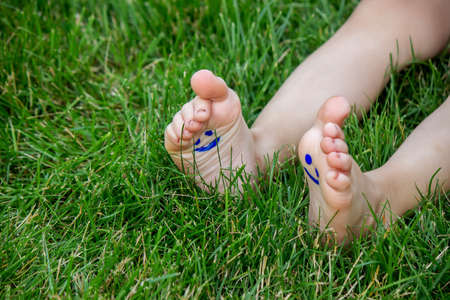 The child was lying on the green grass. Smile with paints on the legs and arms. Child having fun outdoors in the spring park. Selective focus. Natureの写真素材