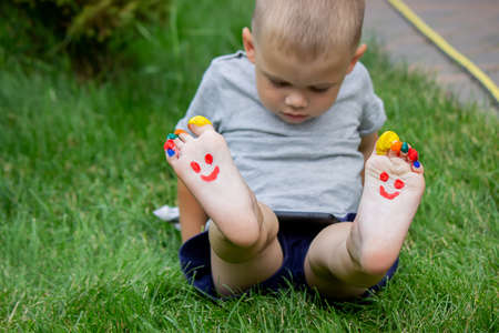 The child was lying on the green grass. Smile with paints on the legs and arms. Child having fun outdoors in the spring park. Selective focus. Natureの写真素材