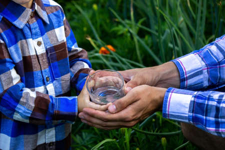 water in a glass in the hands of a child and father. Nature. Selective focusの写真素材