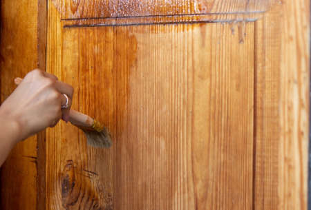 Beautiful young girl paints a wooden door. Summer work in the garden. Selective focusの写真素材