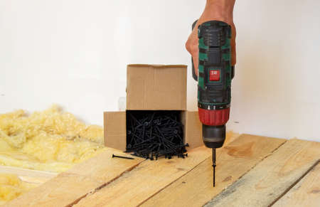 the man twists the screws into the board. Repair of the floor in the house. Selective focus. Interの写真素材