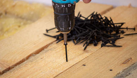 Hand with cordless screwdriver and drill isolated on white background. Twists screws into the board. Selective focusの写真素材