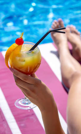 a girl on a sun lounger near the pool drinks a cocktail from a freshly squeezed orange.の写真素材