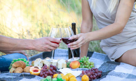 picnic in nature, a girl and a man are holding glasses in their hands with wine. Selective focusの写真素材