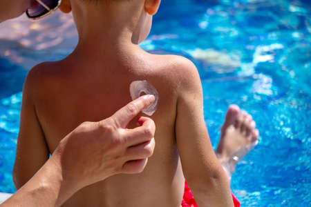 Mother puts cream on her son's back. Caring for baby skin. Sunscreens in the travelの写真素材