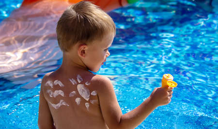 Mother puts cream on her son's back. Caring for baby skin. Sunscreens in the travelの写真素材