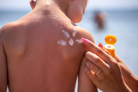 Mother puts cream on her son's back. Caring for baby skin. Sunscreens in the travel. selective focusの写真素材