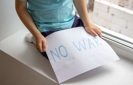 a little boy is holding a piece of paper on which is written no to war. selective focusの写真素材