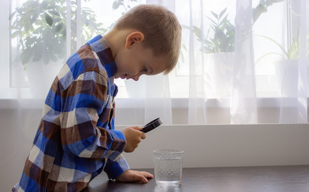 The child examines the water with a magnifying glass in a glass. selective focus. kid.の写真素材