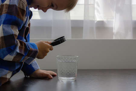 The child examines the water with a magnifying glass in a glass. selective focus. kid.の写真素材