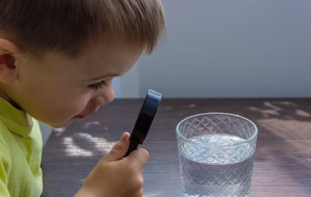 The child examines the water with a magnifying glass in a glass. selective focus. kid.