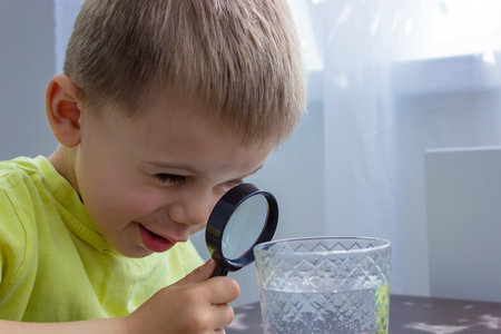 The child examines the water with a magnifying glass in a glass. selective focus. kid.の写真素材