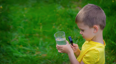 The child examines the water with a magnifying glass in a glass. selective focus. kid.の写真素材