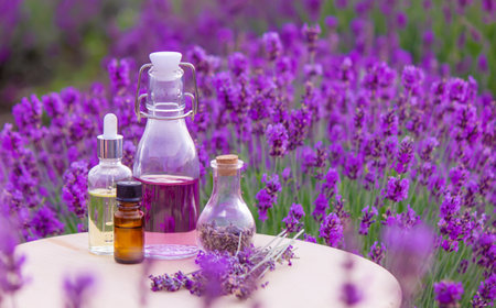 A bottle of lavender essential oil on a wooden table and a field of flowers background. selective focusの写真素材