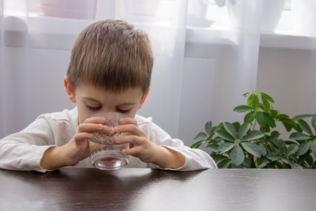 Cute little boy drinks water from a glass. selective focusの写真素材