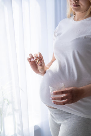 Pregnant woman drinks omega three. selective focus. White.の写真素材