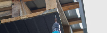 a man repairs the roof, tightens the self-tapping screw with a screwdriver. selective focus