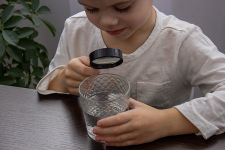 A child looks at the water through a magnifying glass. Selective focus.の写真素材