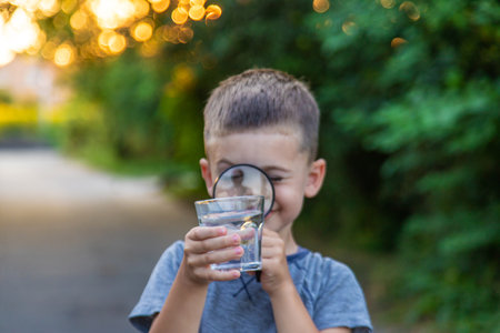 A child looks at the water through a magnifying glass against the background of nature.の写真素材
