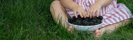little girl eats blackberry on the background of nature. Selective focus.の写真素材