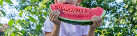 the boy eats a watermelon on the background of the garden. Selective focus.の写真素材