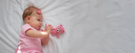 A baby in a pink dress lies with a pink teddy bear on a white background.baby.の写真素材
