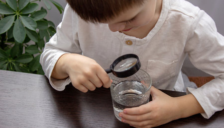 little boy looking at water through a magnifying glass, water analysis. Selective focusの写真素材