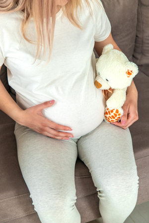 Pregnant woman and white teddy bear. Selective focus. Cute.