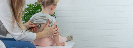 Female doctor examining little girl, listening to lungs with stethoscope. Pediatrician's...