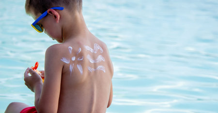 A boy applies sunscreen against the background of a swimming pool. Suntan lotionの写真素材