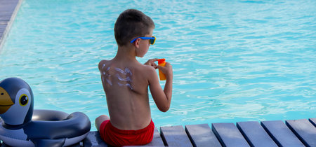 A boy applies sunscreen against the background of a swimming pool. Suntan lotion