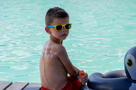 A boy applies sunscreen against the background of a swimming pool. Suntan lotionの写真素材