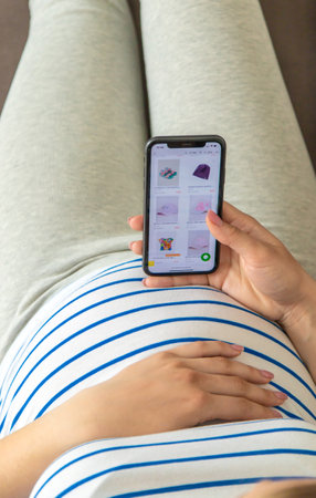 Pregnant woman on the phone in the online store for baby clothing. Selective focus. Cute.の写真素材