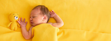 Newborn baby girl sleeping on a yellow background with a yellow teddy bearの写真素材