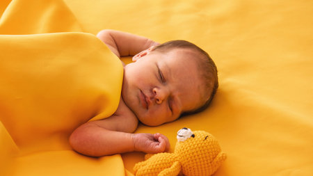 Newborn baby girl sleeping on a yellow background with a yellow teddy bear