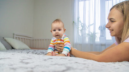 Cute little girl and her mother playing in the bedroom on the bed. Having a good time at home