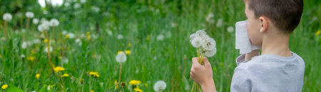 The boy has allergies. He is blowing on a dandelion.