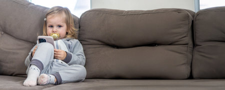 Little girl sitting on the couch using her phone.の写真素材