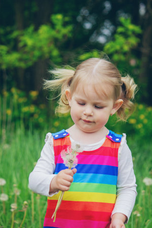 Adorable cute little girl blowing on a dandelion flower on the street in summer.の写真素材
