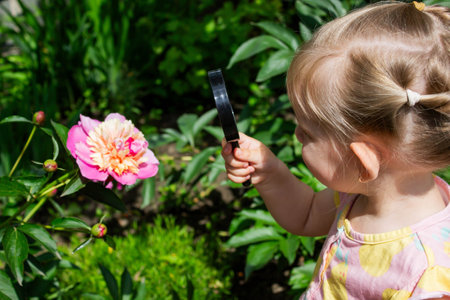 little girl looking at flowers in the garden through a magnifying glass. Selective focus.の写真素材