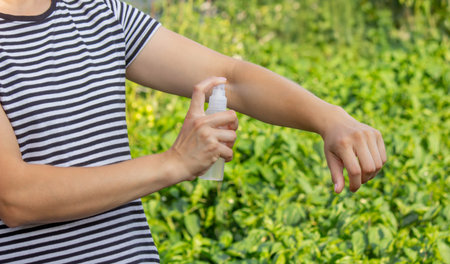 Woman spraying mosquito repellent on arm outdoors in summer garden.の写真素材
