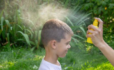 Mother spraying mosquito repellent on child hand outdoors in summer garden.