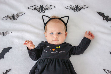 Little girl in a black cat costume on a background of bats, Halloween idea for celebrating...