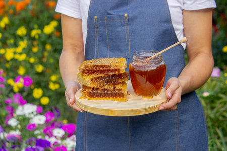 Fresh honey in jar with honeycomb and dipper outdoors.
