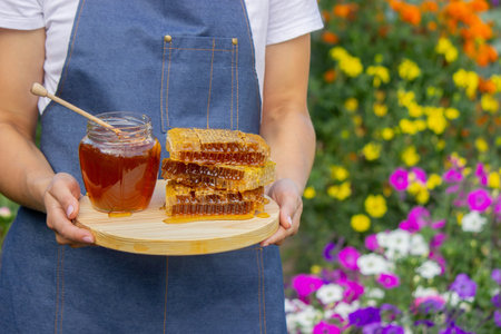 Fresh honey in jar with honeycomb and dipper outdoors.
