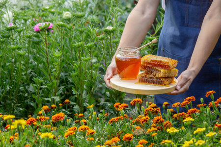Fresh honey in jar with honeycomb and dipper outdoors.