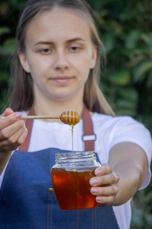 Woman holding a jar of honey on a garden background. Selective focus.