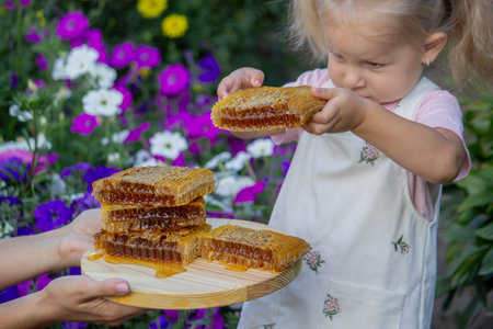 Little Girl Eating Honey with Honeycomb Outdoors.